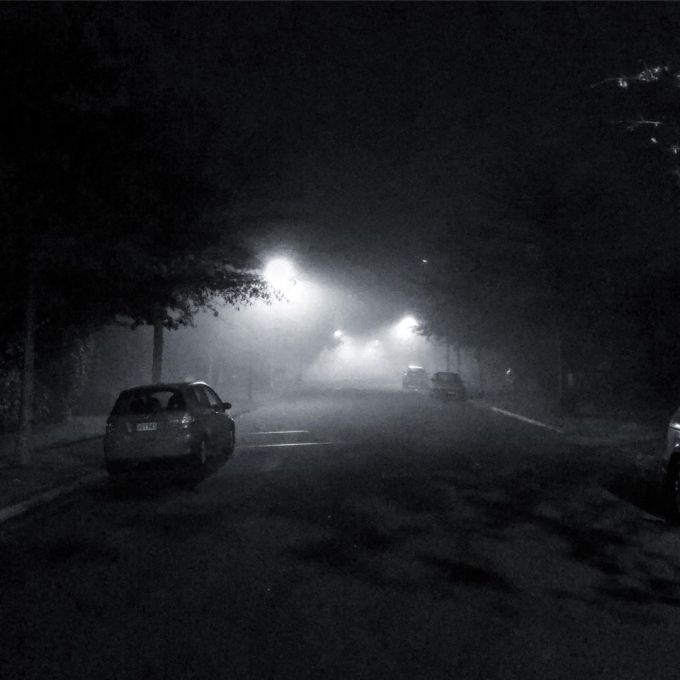 Street lights illuminate the fog and the street during the evening