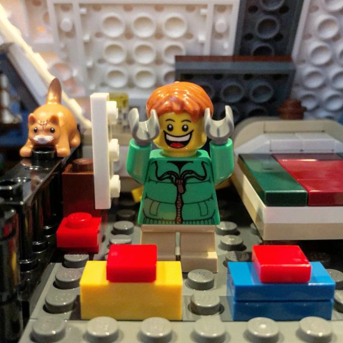 Lego boy figure celebrating with presents in the bedroom of the Lego Winter Village Cottage with Lego Jack the Cat on the balcony railing