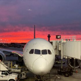 Air New Zealand plane at boarding gate at O'Hare International Airport Terminal 5 with a red sunset in the background