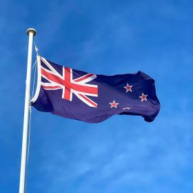 The New Zealand flag waves in the breeze with a blue sky behind it