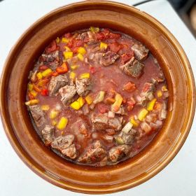 Beef, onions, red peppers, yellow peppers, tomato pieces in a tomato sauce in a crockpot