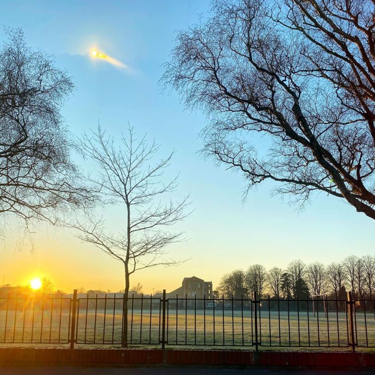 Sunrise over a boys' high school and its grounds with frost on it with a crisp blue sky and barren trees