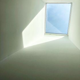 White skylight shaft somewhat in shadow leading to the skylight above with light blue sky beyond