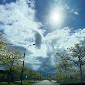 Blue skies leading towards dark clouds in the distance with bright green spring leaves on the trees