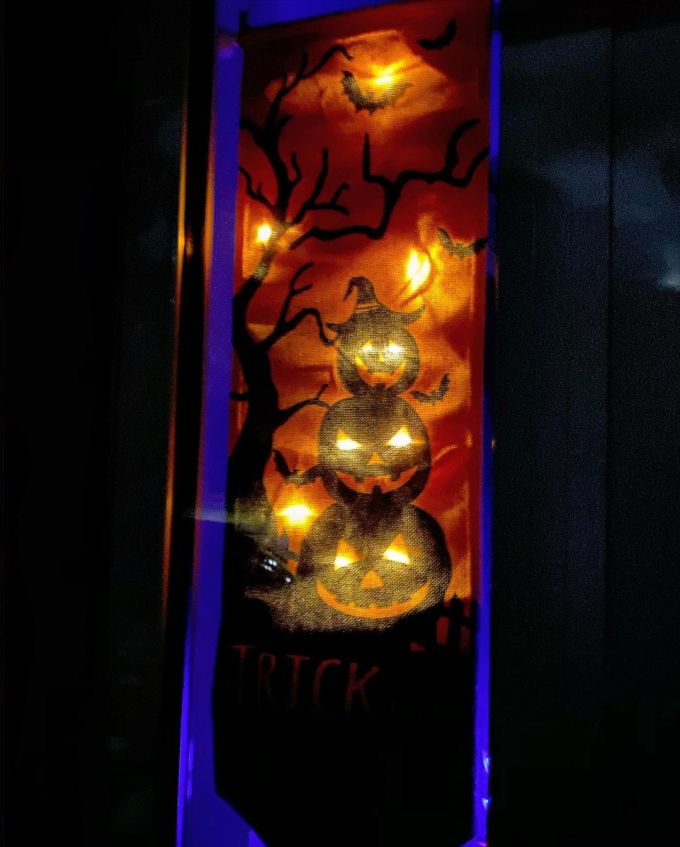 Halloween banner lit up with orange LED lights so Jack-O'-Lantern eyes glow and orange stars are in the sky with bats flying around