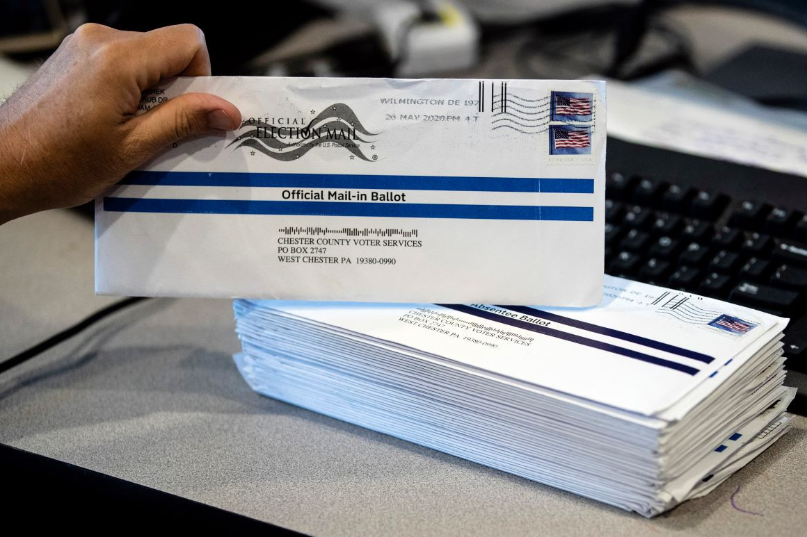 Person holds up an official mail-in ballot for the American General Election for 2020 with a pile of postmarked envelopes on the table beside it