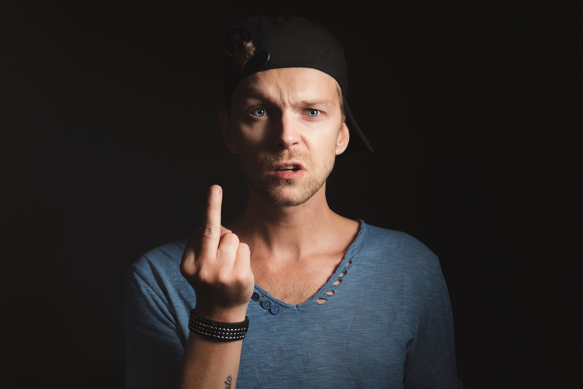 Man in a baseball cap with one eyebrow arched and the middle finger extended