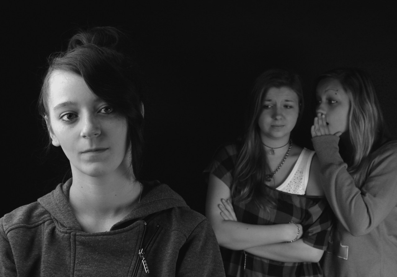 Two girls in the background gossip about the girl in the foreground