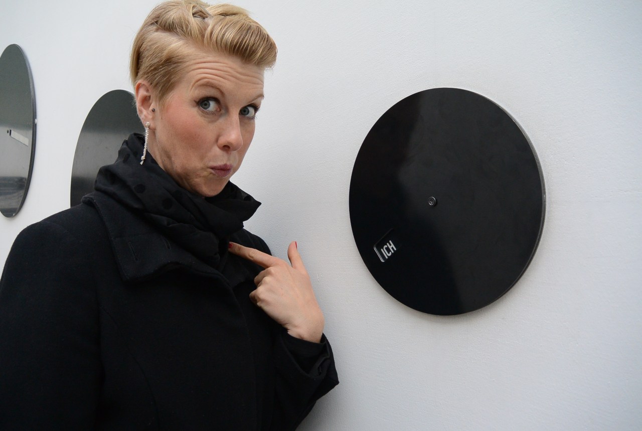 Woman points to herself, standing next to a clock that says "Ich" ("I") in German