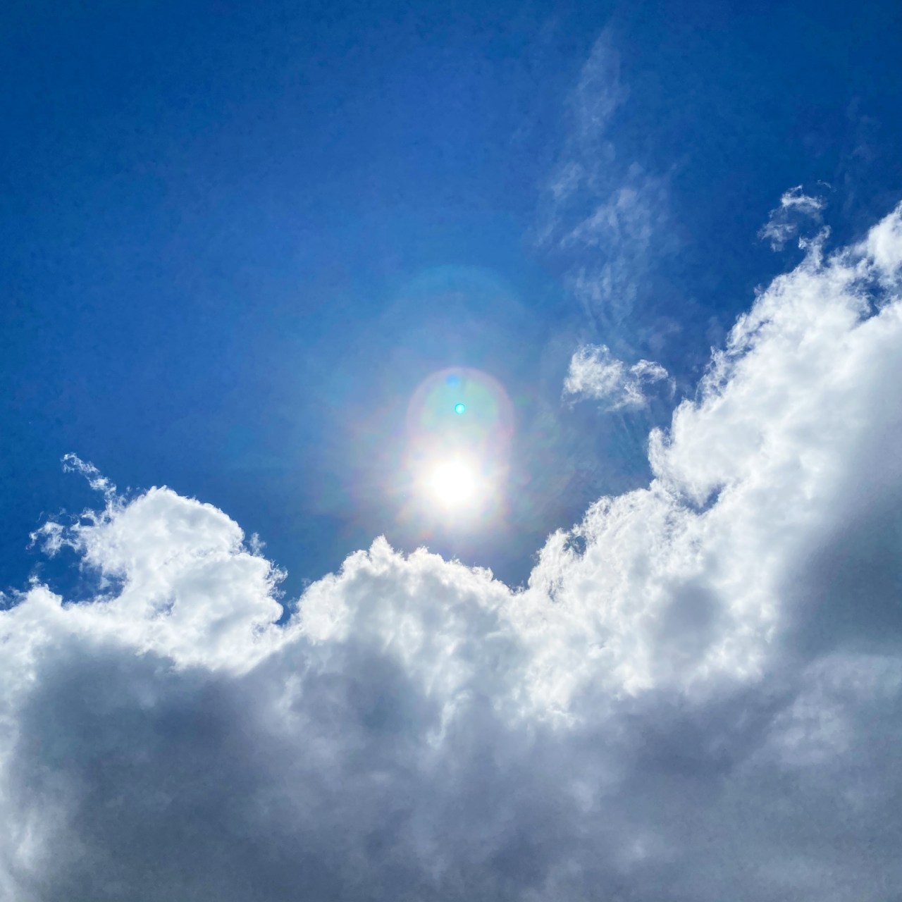 The sun shines down with blue skies behind it and clouds in the foreground