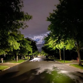 Slick suburban street with leafy green oak trees either side, the breaking clouds illuminated by the moon, after days of rain in the summer
