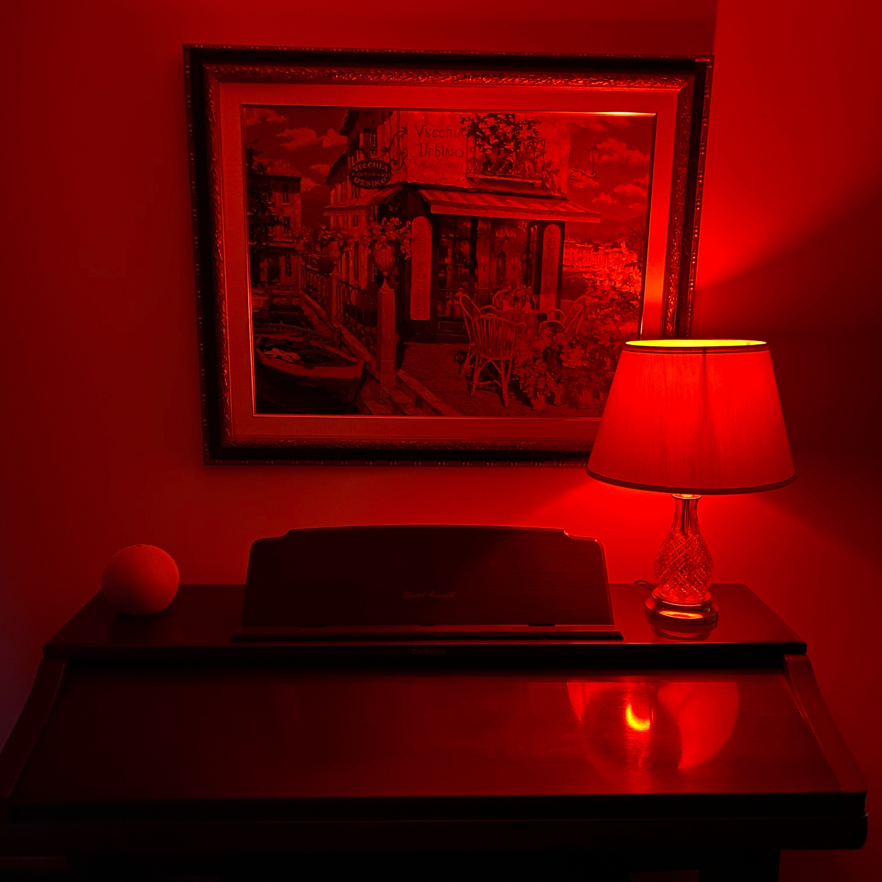 Lamp with a red light makes the painting, wall, and organ in the room red