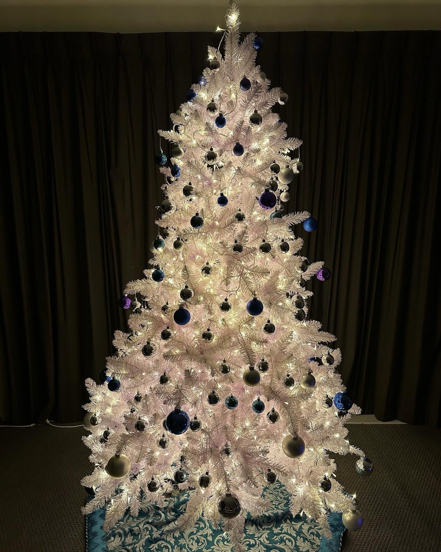 A white Christmas tree with warm white lights and blue and silver ornaments illuminating a room