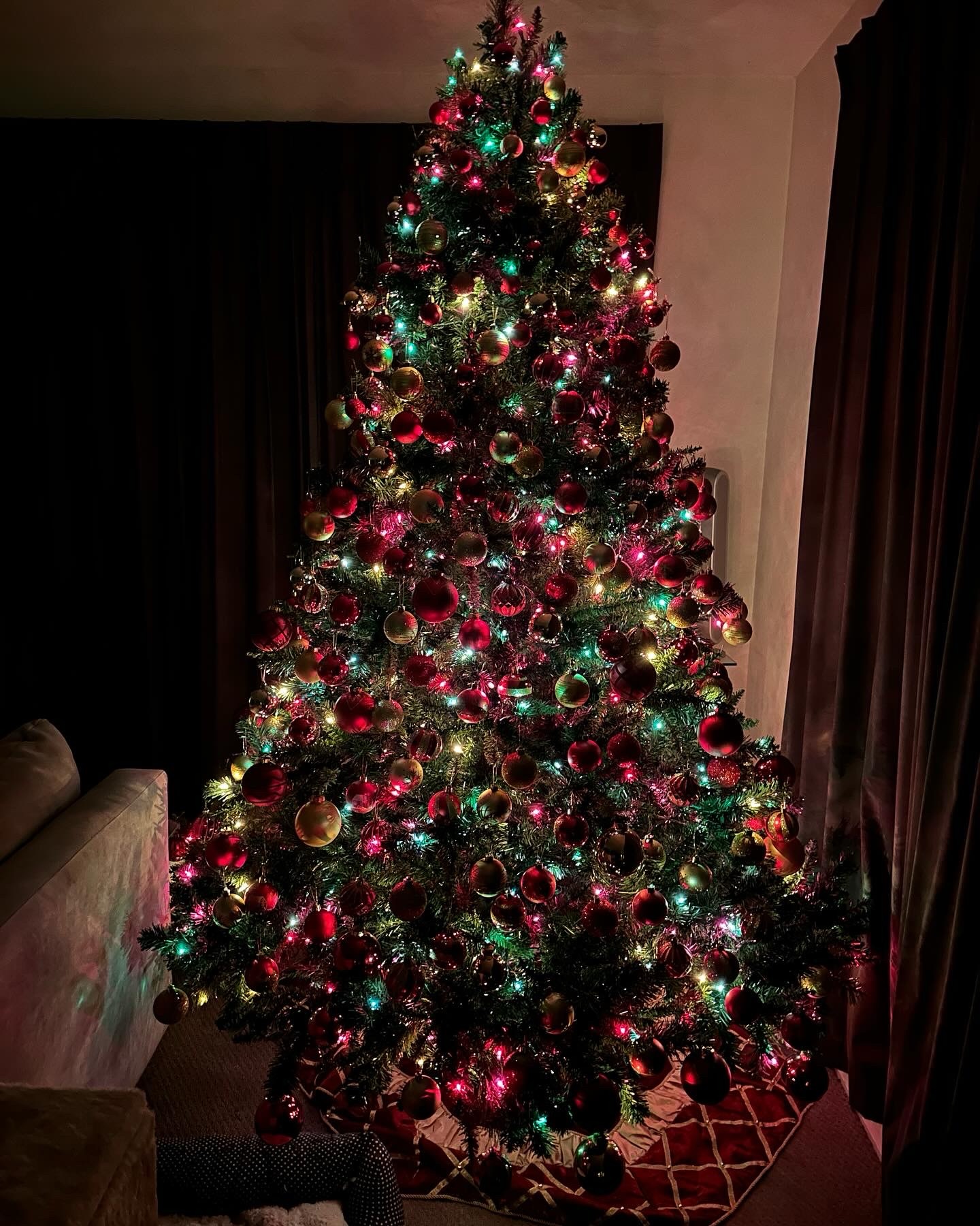 A green Christmas tree with multicolor lights and red and gold ornaments illuminating a room